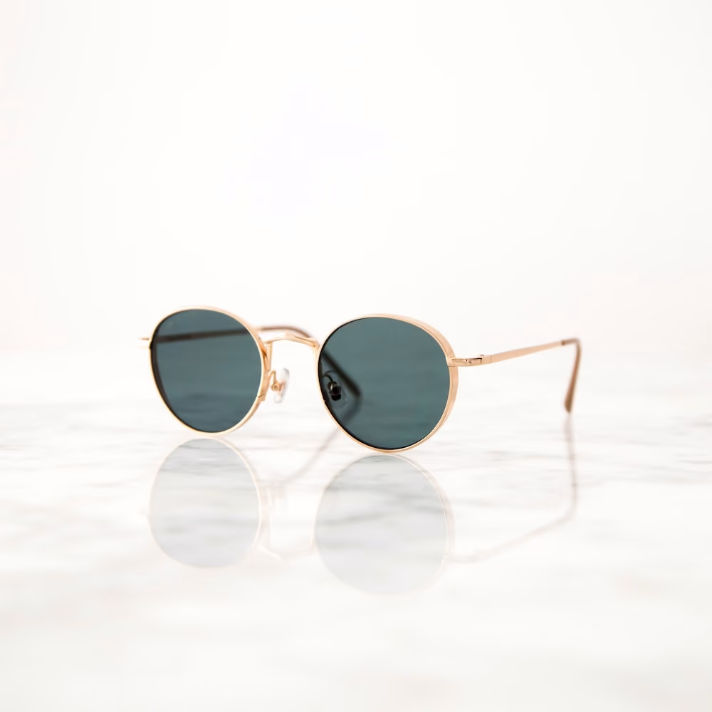 A pair of round sunglasses with a gold frame and dark lenses is shown against a white background.