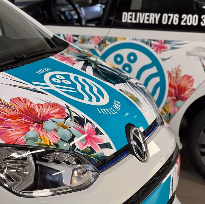 Close-up of white Volkswagen cars with bright floral and blue logo decals on the hood and side.