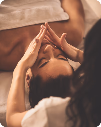 A person receiving a facial massage while lying down with eyes closed and a towel on their chest.
