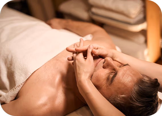 Man lying down receiving a facial massage with hands gently pressing around his nose and eyes.
