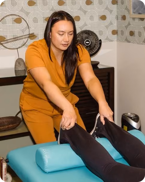 Therapist in orange outfit stretching a person's legs on a teal therapy table.