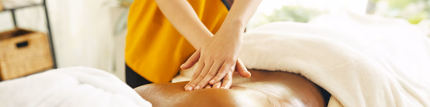 Massage therapist pressing hands on back of person lying on a massage table with a white towel.