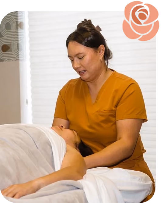 Massage therapist in an orange uniform massaging a client lying on a table covered in white sheets.