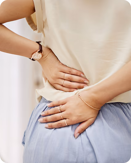 Person wearing beige top and blue skirt holding lower back and abdomen in pain.
