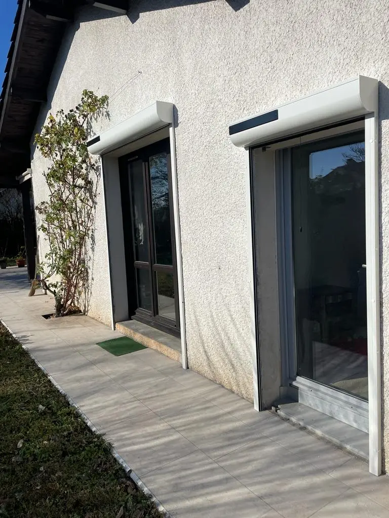 Entrée d'une maison moderne avec portillon en métal noir et chemin pavé sur herbe verte.