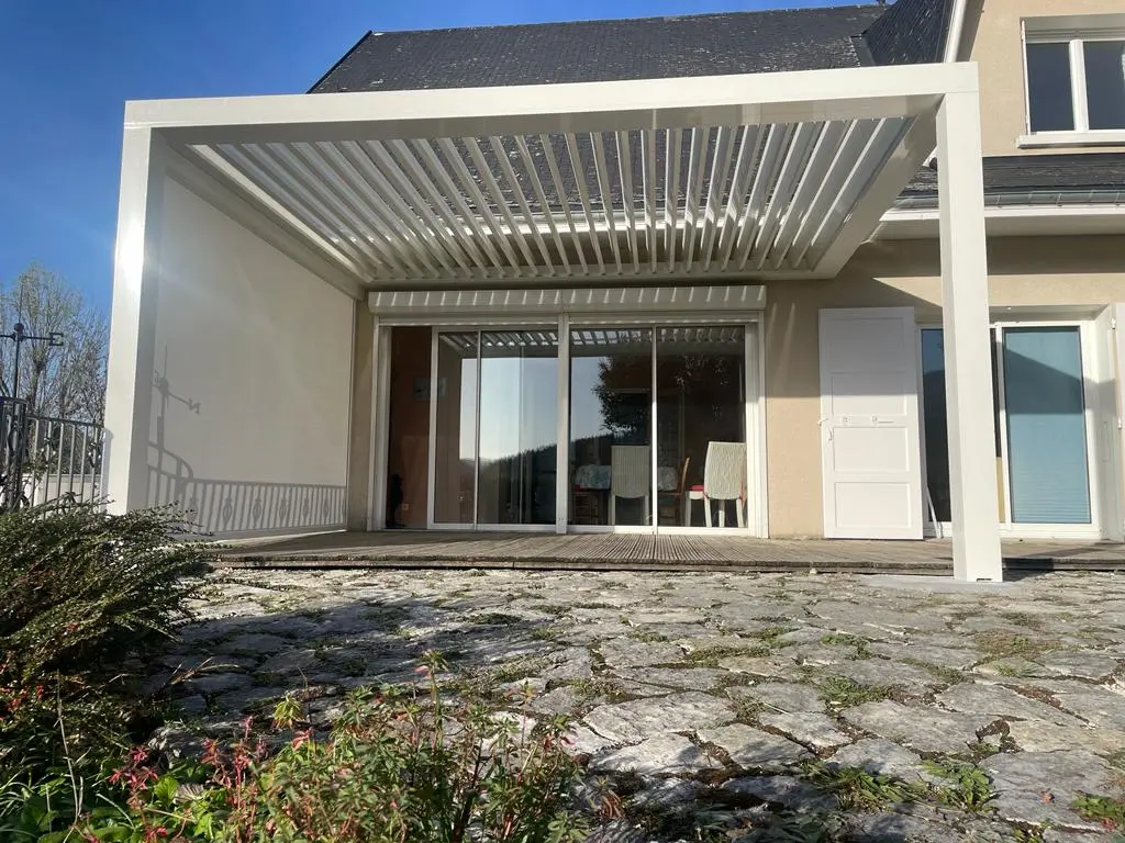 Entrée d'une maison moderne avec portillon en métal noir et chemin pavé sur herbe verte.