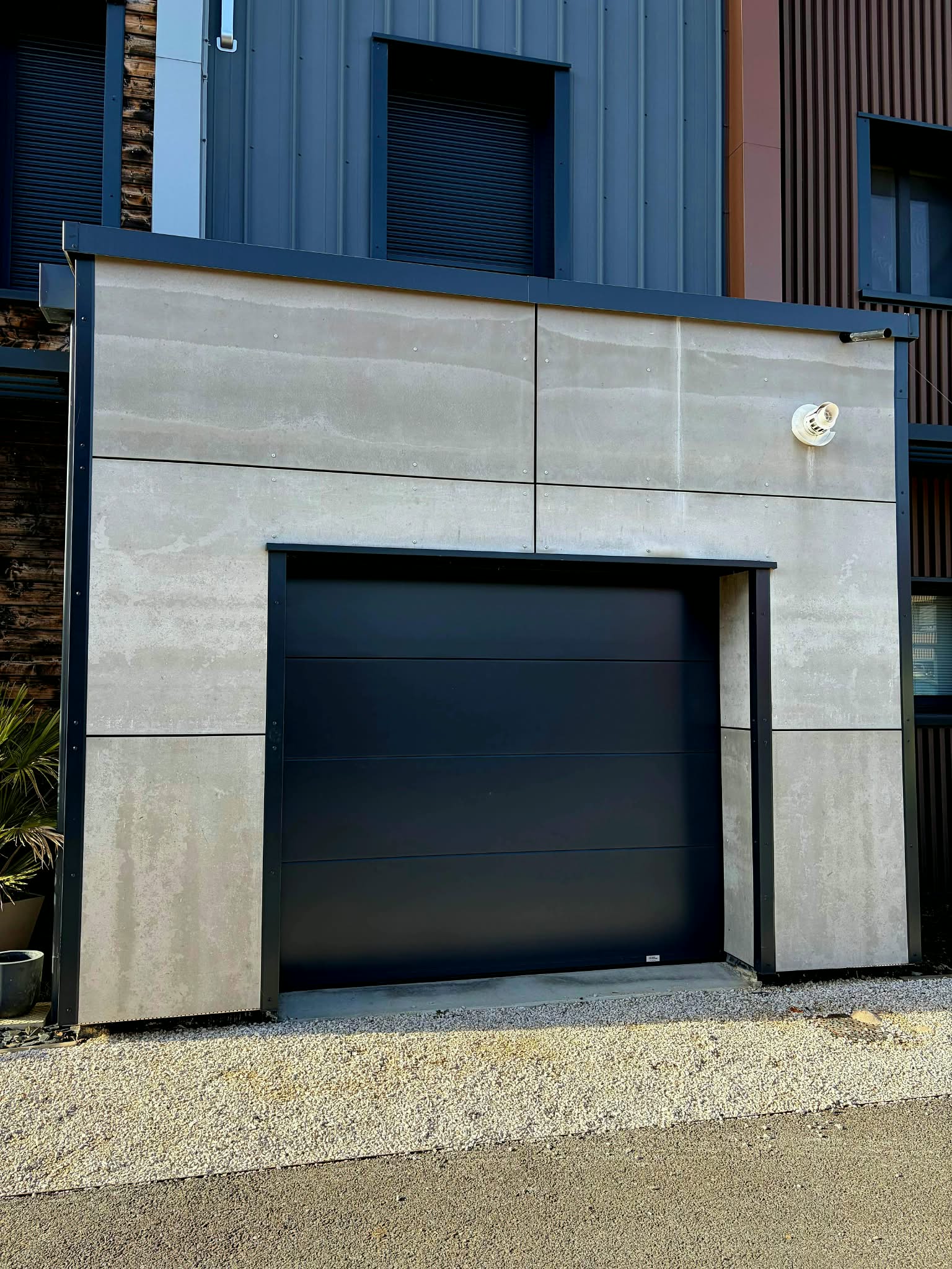 Entrée d'une maison moderne avec portillon en métal noir et chemin pavé sur herbe verte.