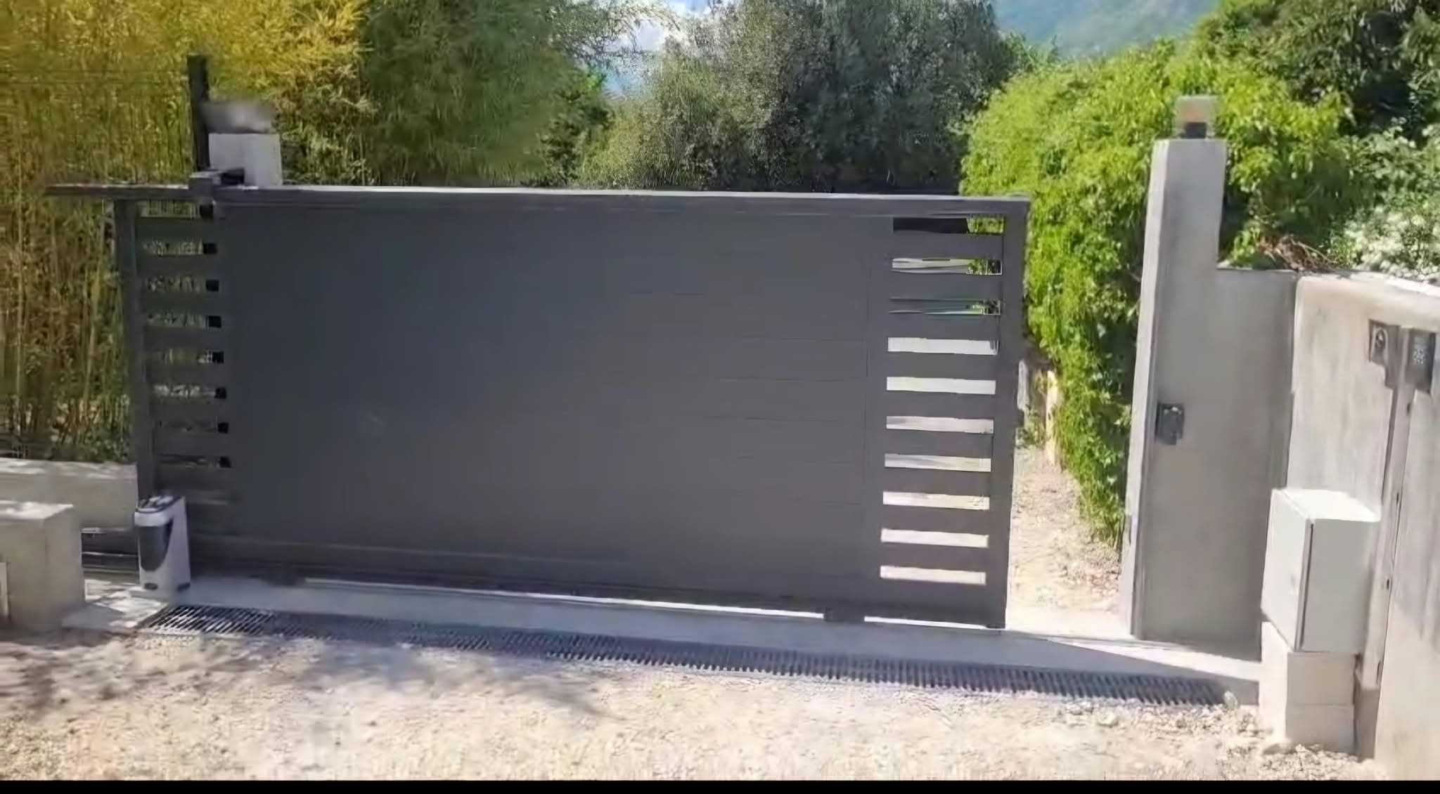 Entrée d'une maison moderne avec portillon en métal noir et chemin pavé sur herbe verte.