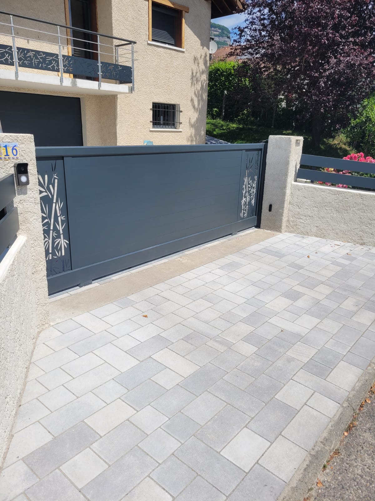 Entrée d'une maison moderne avec portillon en métal noir et chemin pavé sur herbe verte.