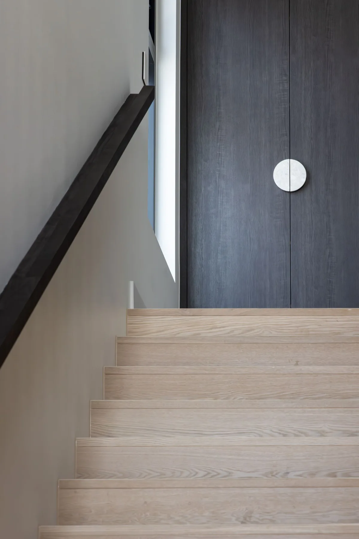 Oak staircase rising to dark timber doors with a round stone handle at 9 Netherby
