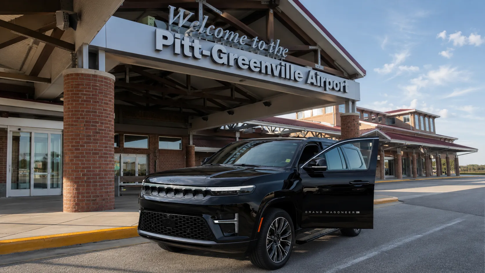 Black Jeep Grand Wagoneer with open door parked under Pitt-Greenville Airport entrance sign.