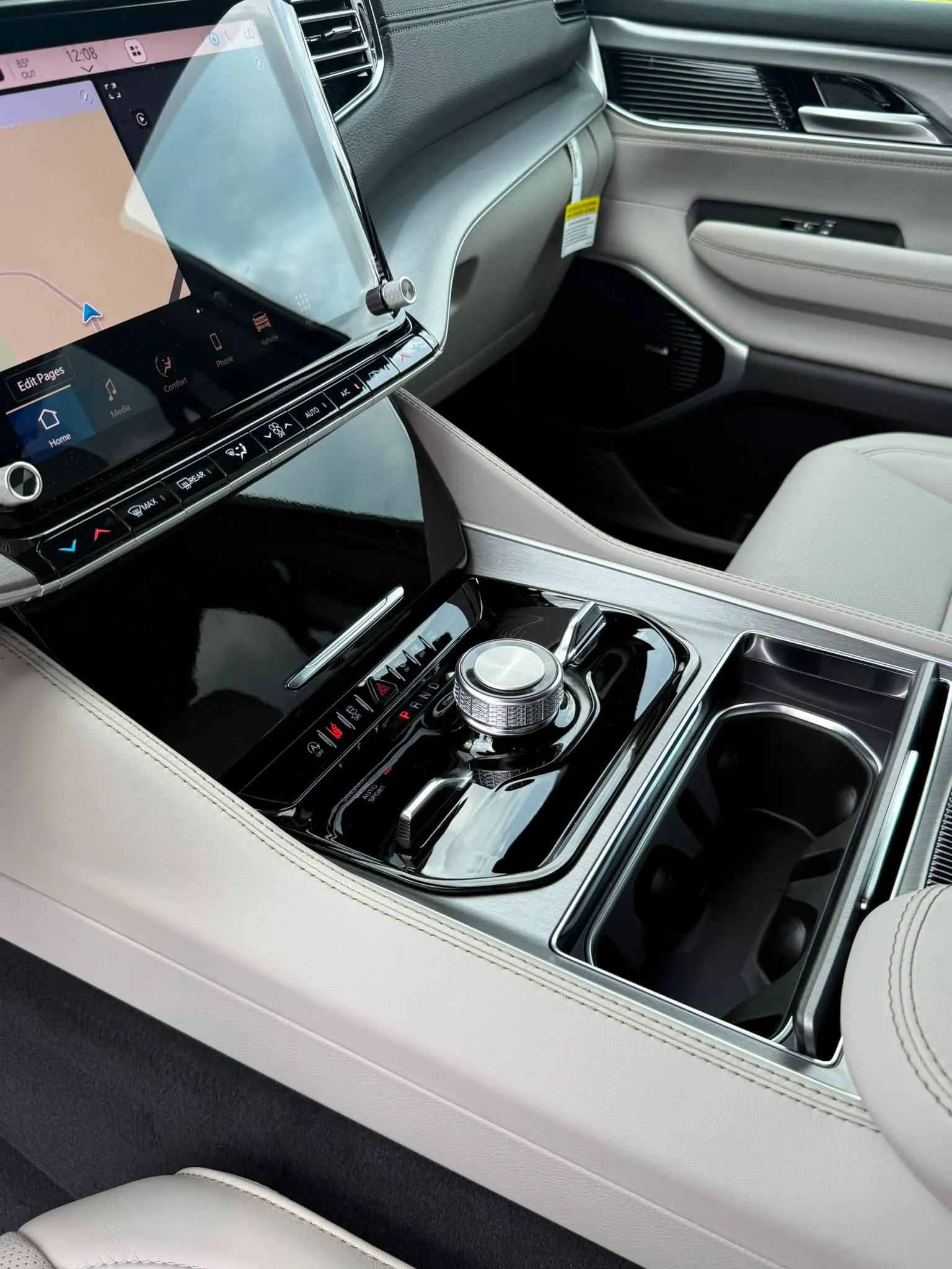 Jeep Grand Wagoneer interior center console with touchscreen, gear selector dial, control buttons, and cup holders.