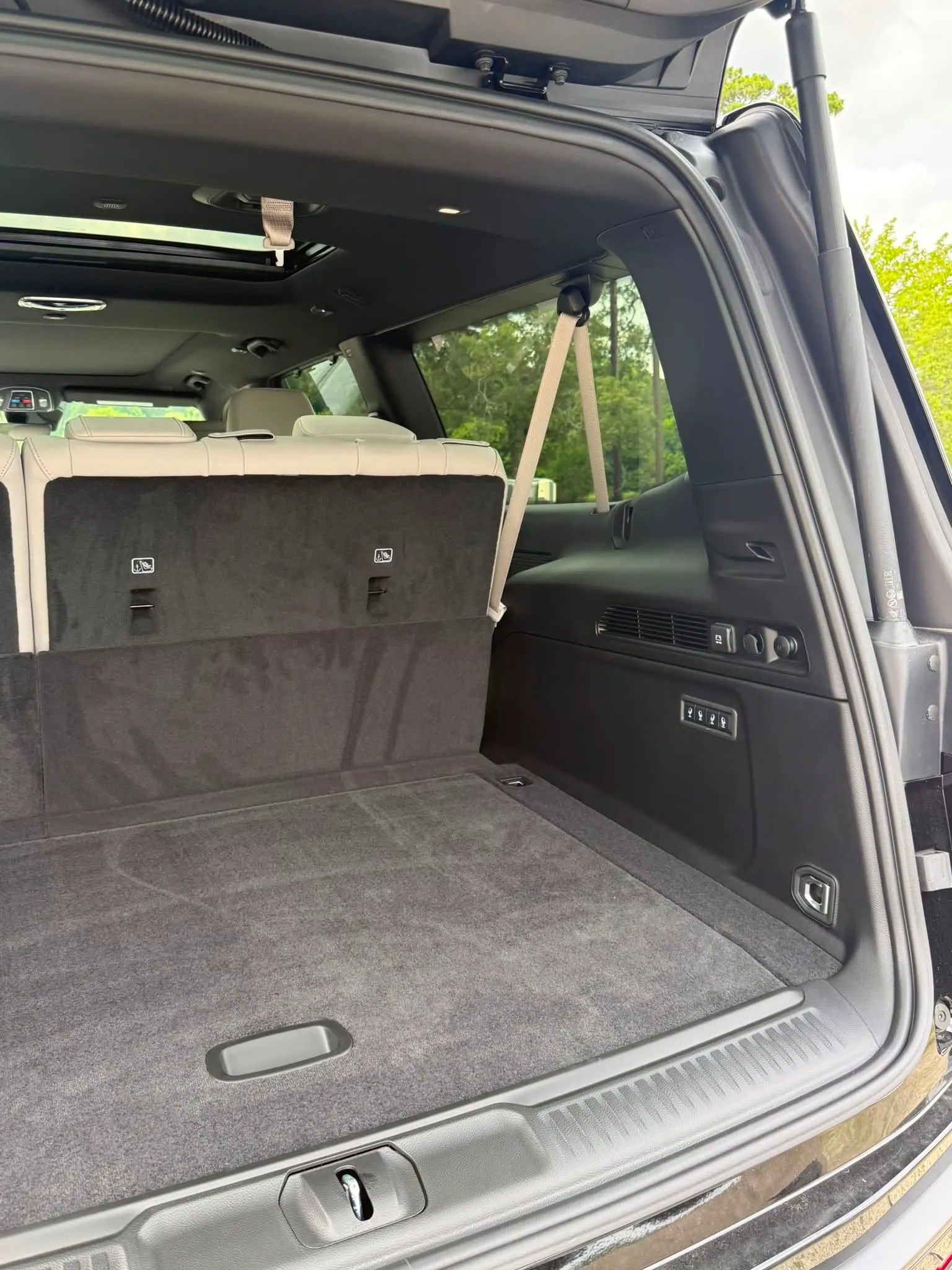 Empty rear cargo area of a black Jeep Grand Wagoneer with beige seats and controls on the side panel.