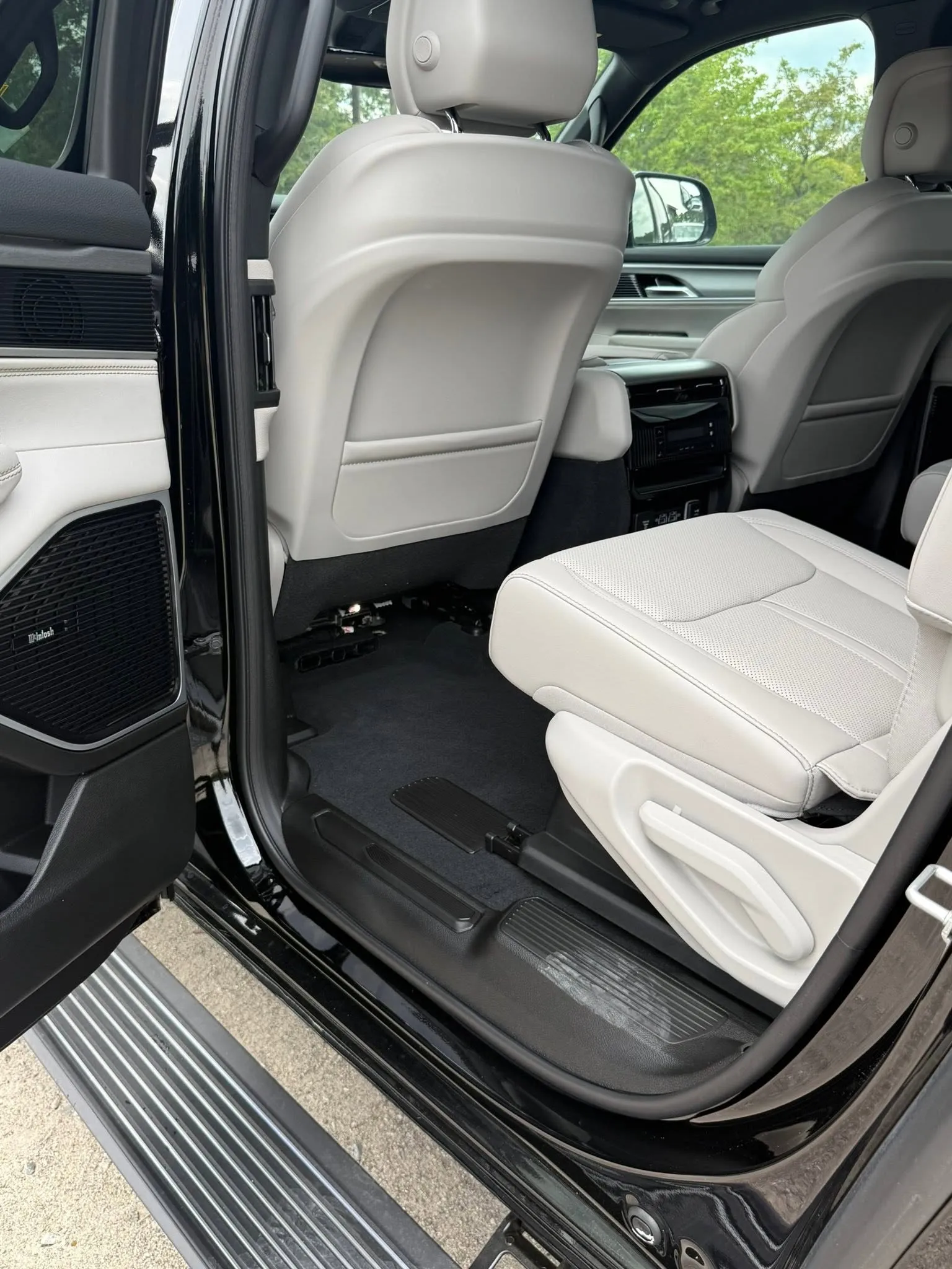 Interior view of a Jeep Grand Wagoneer's rear passenger seat with light leather upholstery and door open.
