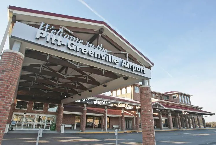 Entrance to Pitt-Greenville Airport building with welcome sign and brick columns under clear blue sky.
