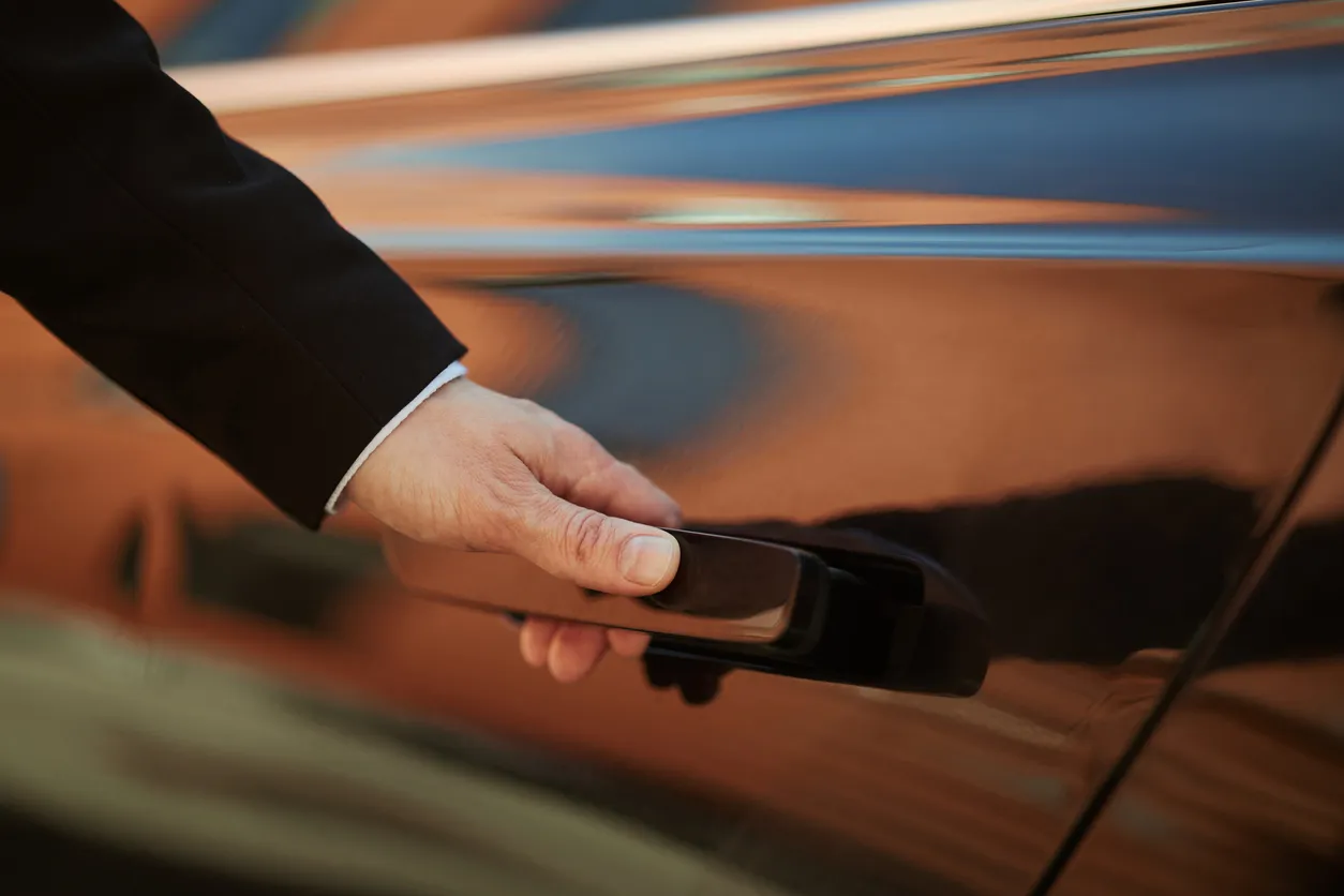 Person in black jacket opening black car door by the handle.