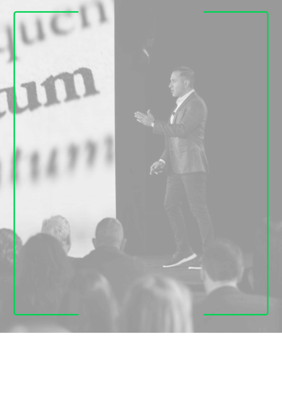 A man in a suit jacket and sneakers is speaking on stage before an audience, gesturing with his hands, with a large close-up projected showing part of the word 'um'.