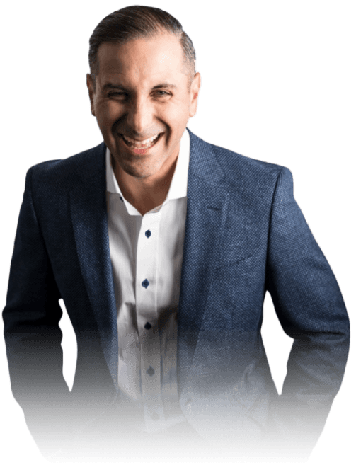 Smiling man with short dark hair wearing a textured dark blue blazer and white shirt, posing with hands in pockets.