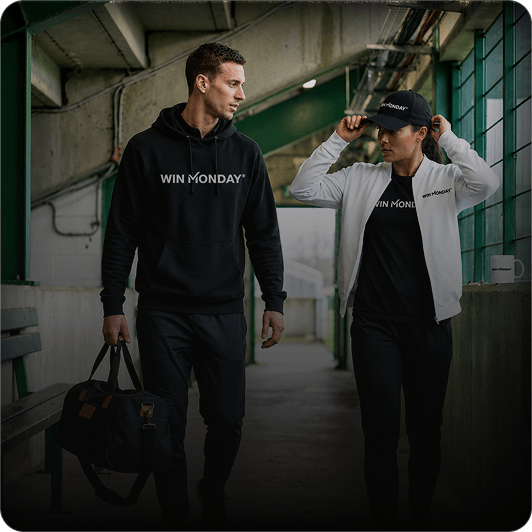 Man and woman walking in industrial corridor wearing black athletic outfits with 'WIN MONDAY' logo; man carries black duffel bag and woman adjusts black cap.