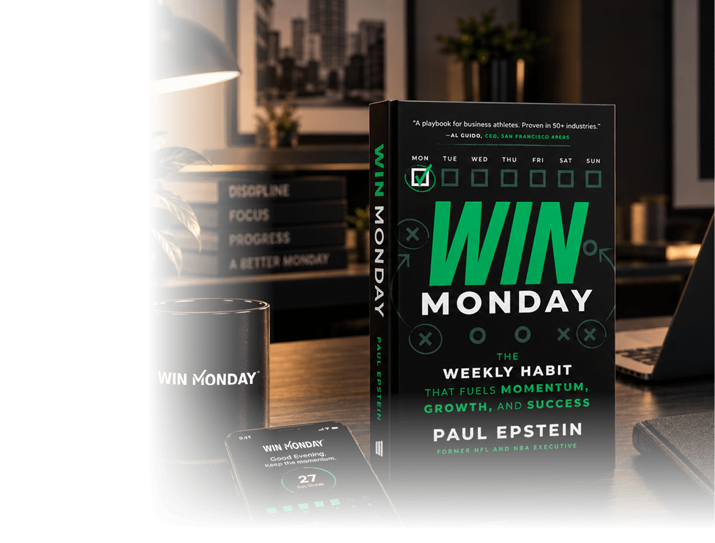 Book titled 'Win Monday' by Paul Epstein, featuring a weekly habit tracker on the cover, placed on a desk with a laptop, a black mug with the book's title, and a phone displaying a progress app screen, with a blurred background showing words: Discipline, Focus, Progress, A Better Monday.