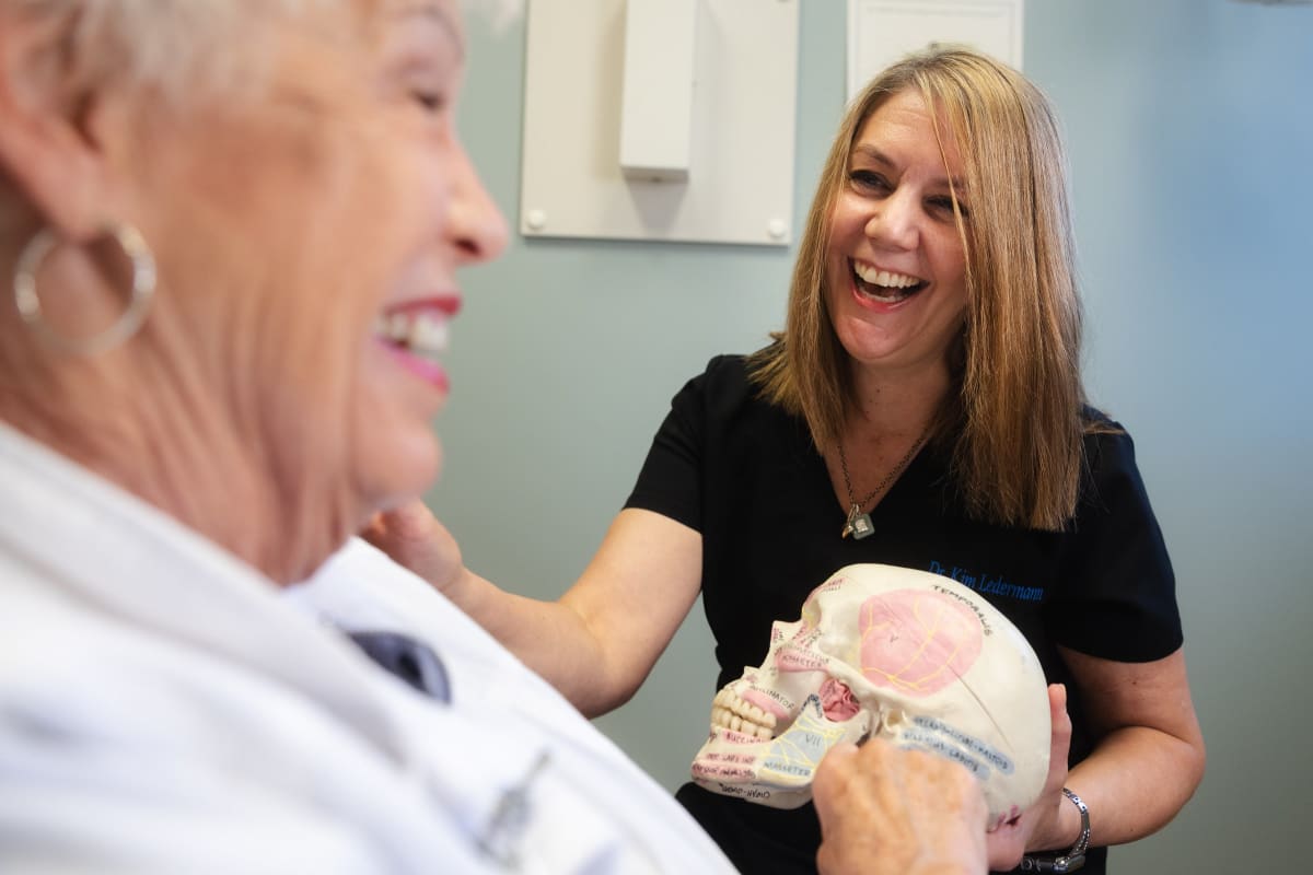 Dentist holding a skull model while discussing TMJ with a patient