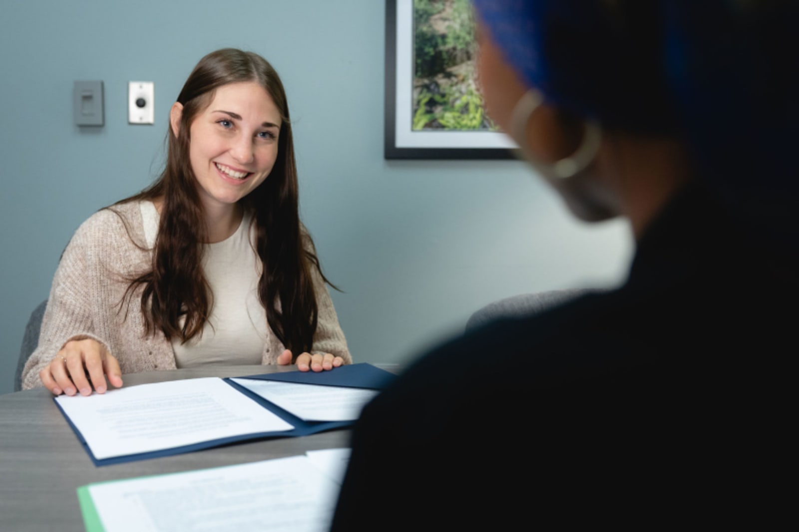 Female dentist consulting with male patient at desk in clinical office setting.