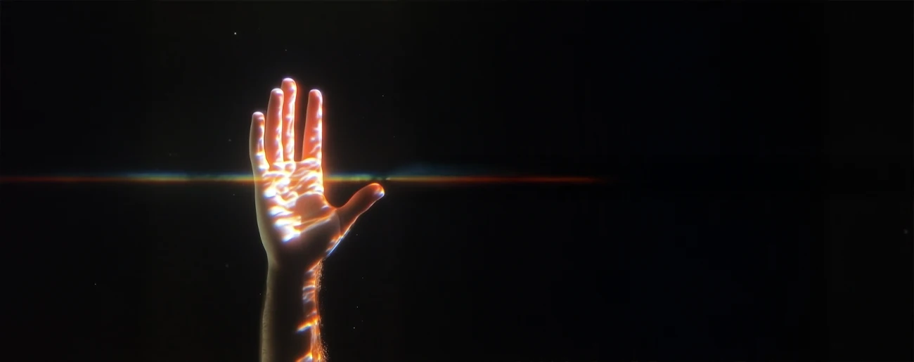 A hand with light reflections is raised against a dark background with a horizontal light streak.