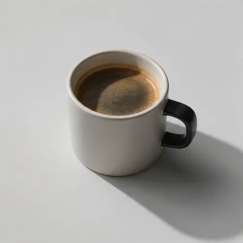 Top view of a black coffee cup with frothy coffee on a light gray surface.