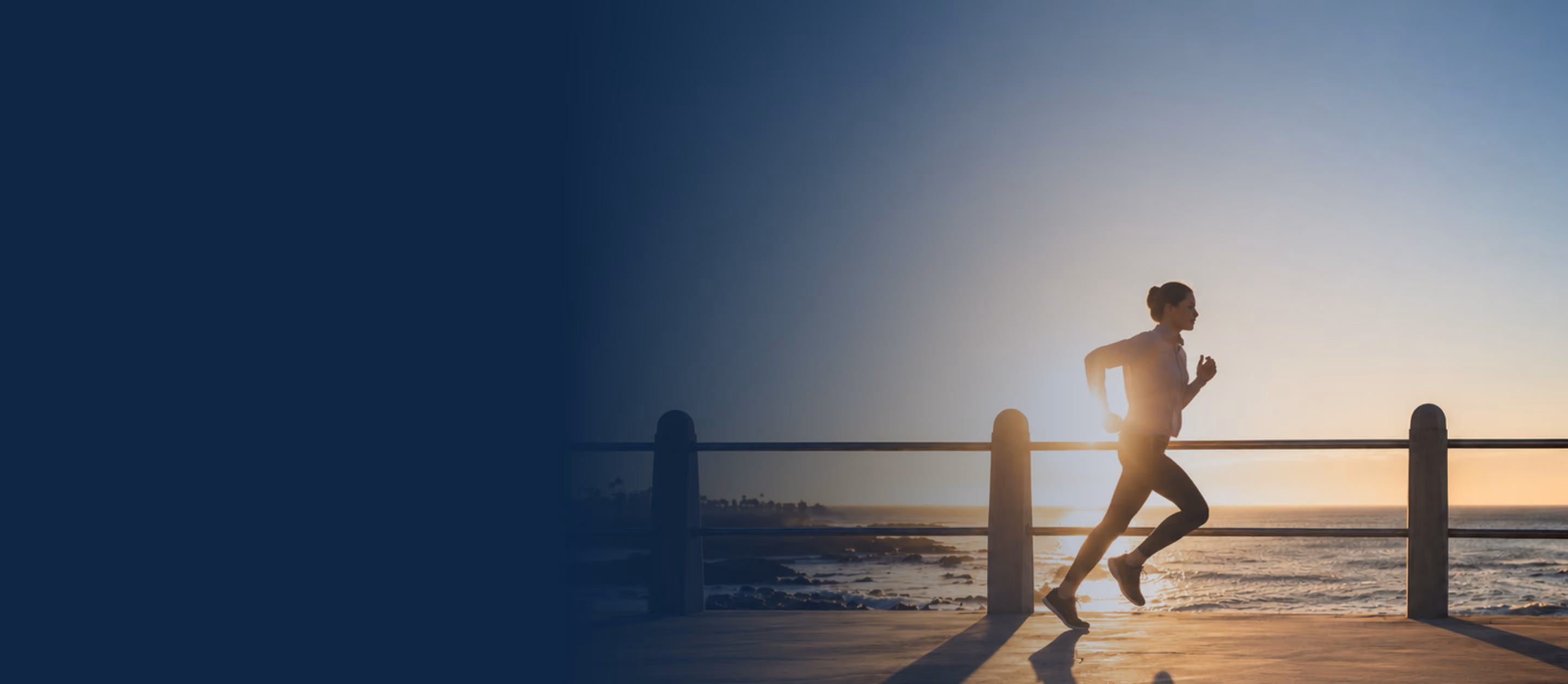 Person jogging on a seaside path at sunset with ocean and railings in the background.