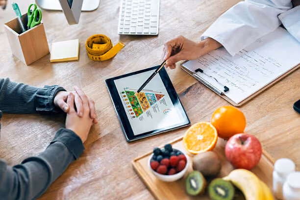 Nutritionist pointing to food group pyramid on tablet while discussing healthy diet with patient.