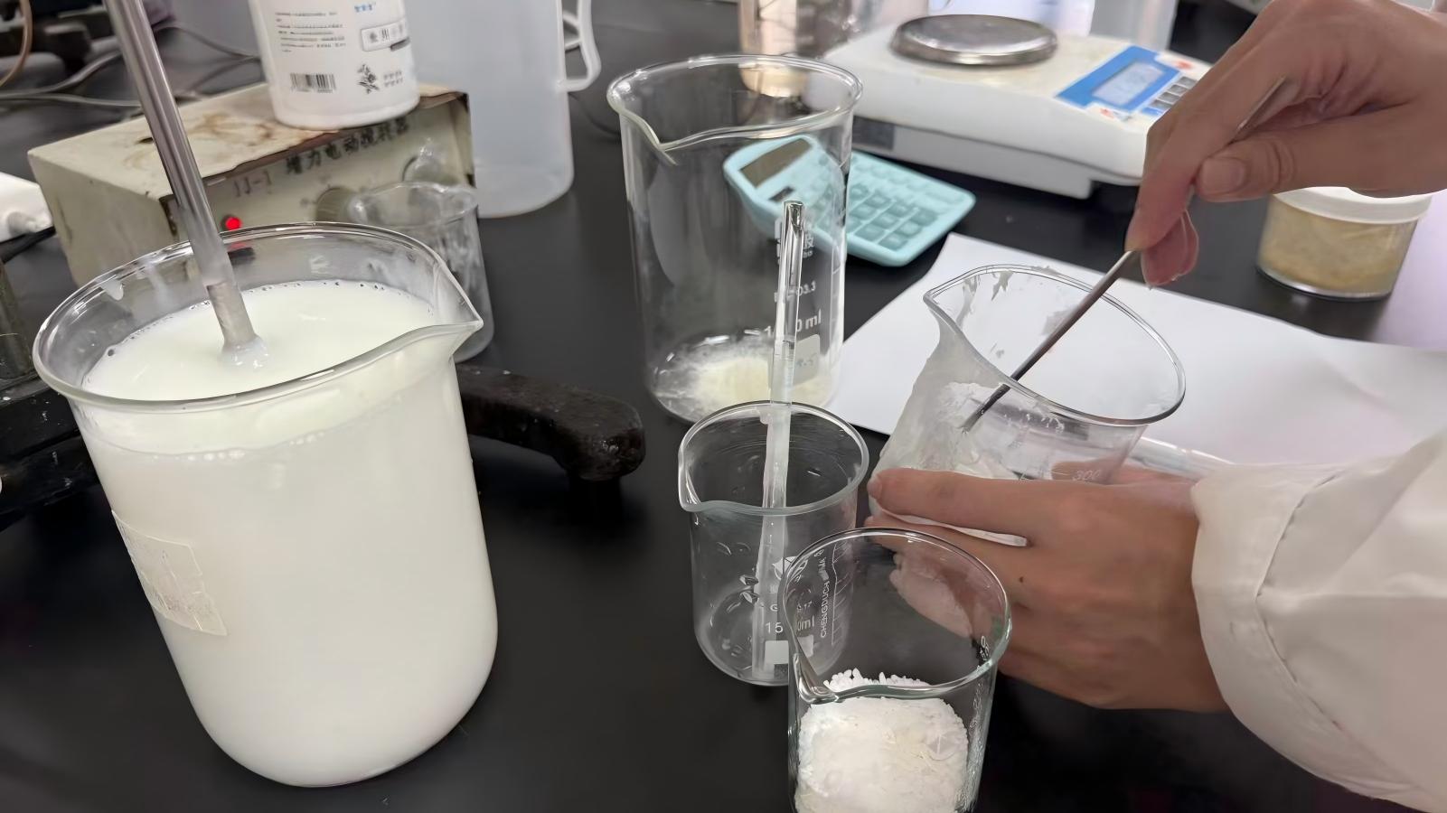 Lab technician weighing powder ingredients into a beaker while mixing a milky cosmetic base