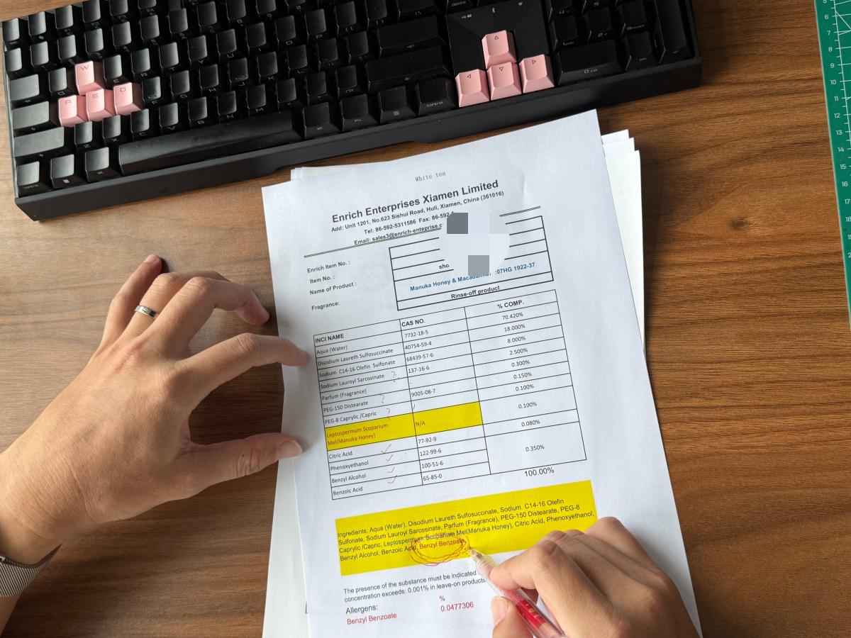 Hand reviewing a cosmetic formula specification sheet with INCI ingredients and percentages highlighted for compliance review