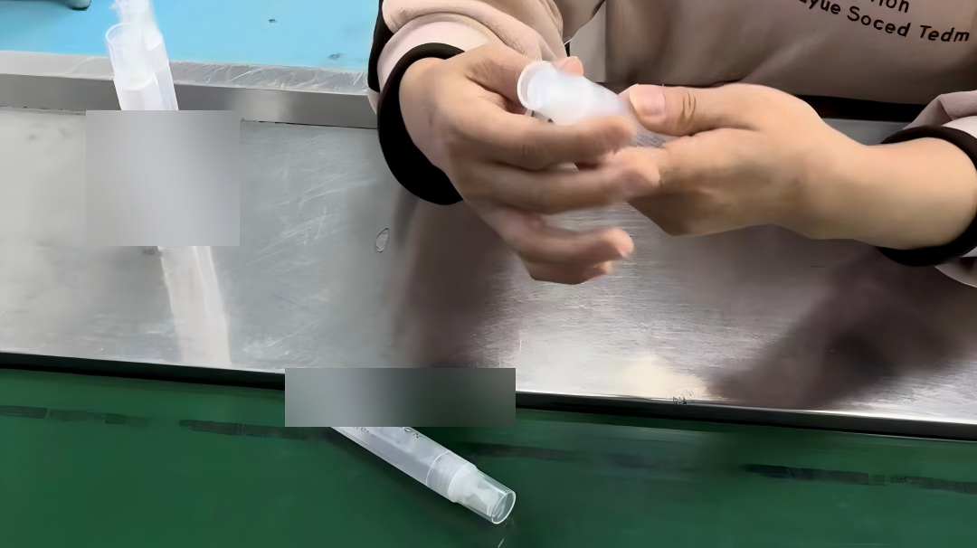 A worker's hands checking a sample bottle at a production line workstation, with a second bottle placed on the conveyor belt for inspection