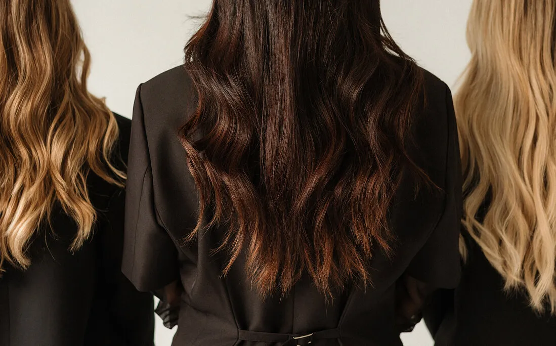 Back view of three women with long wavy hair in different shades wearing black tops.