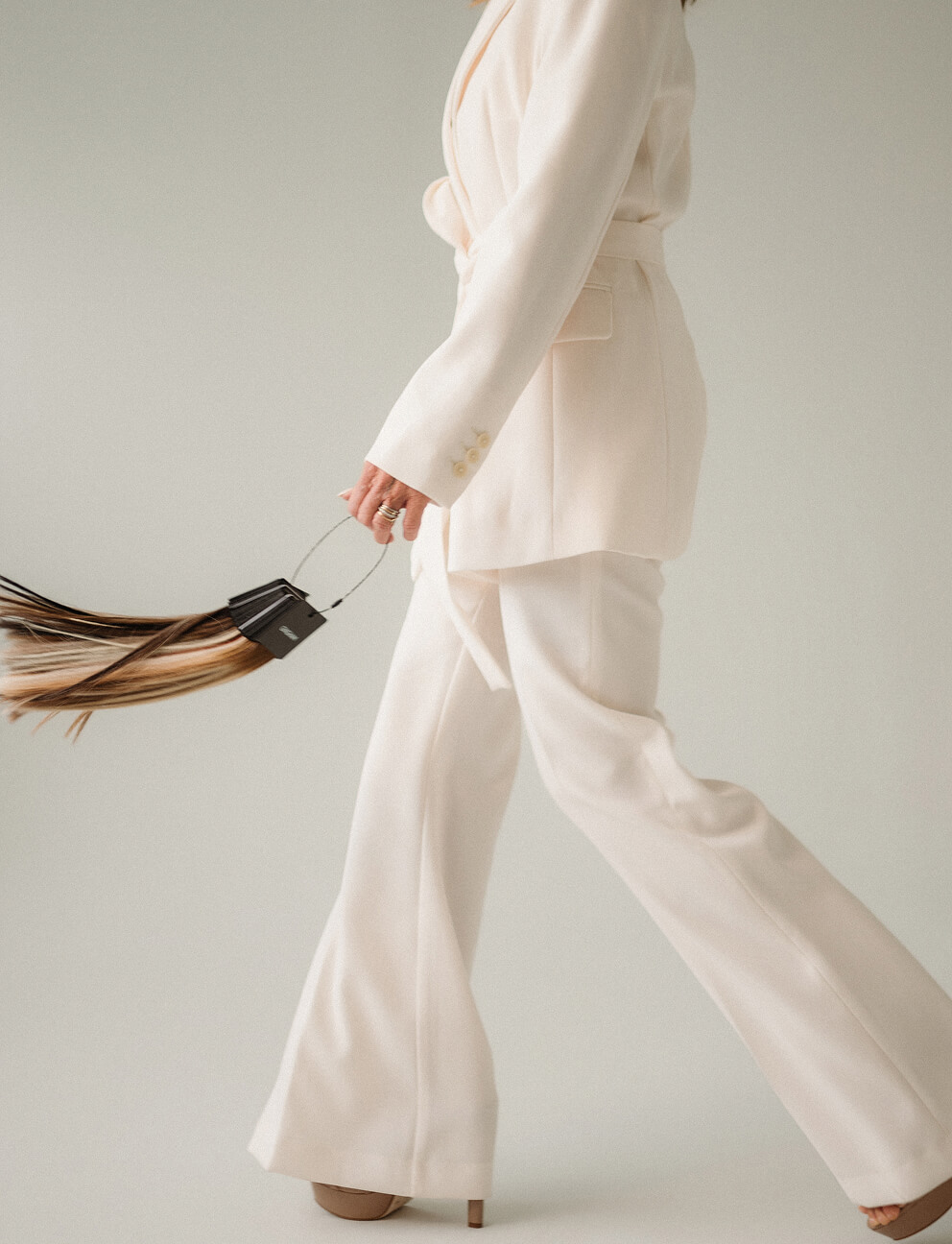 Person walking in cream suit holding hair extension strands with black holder.