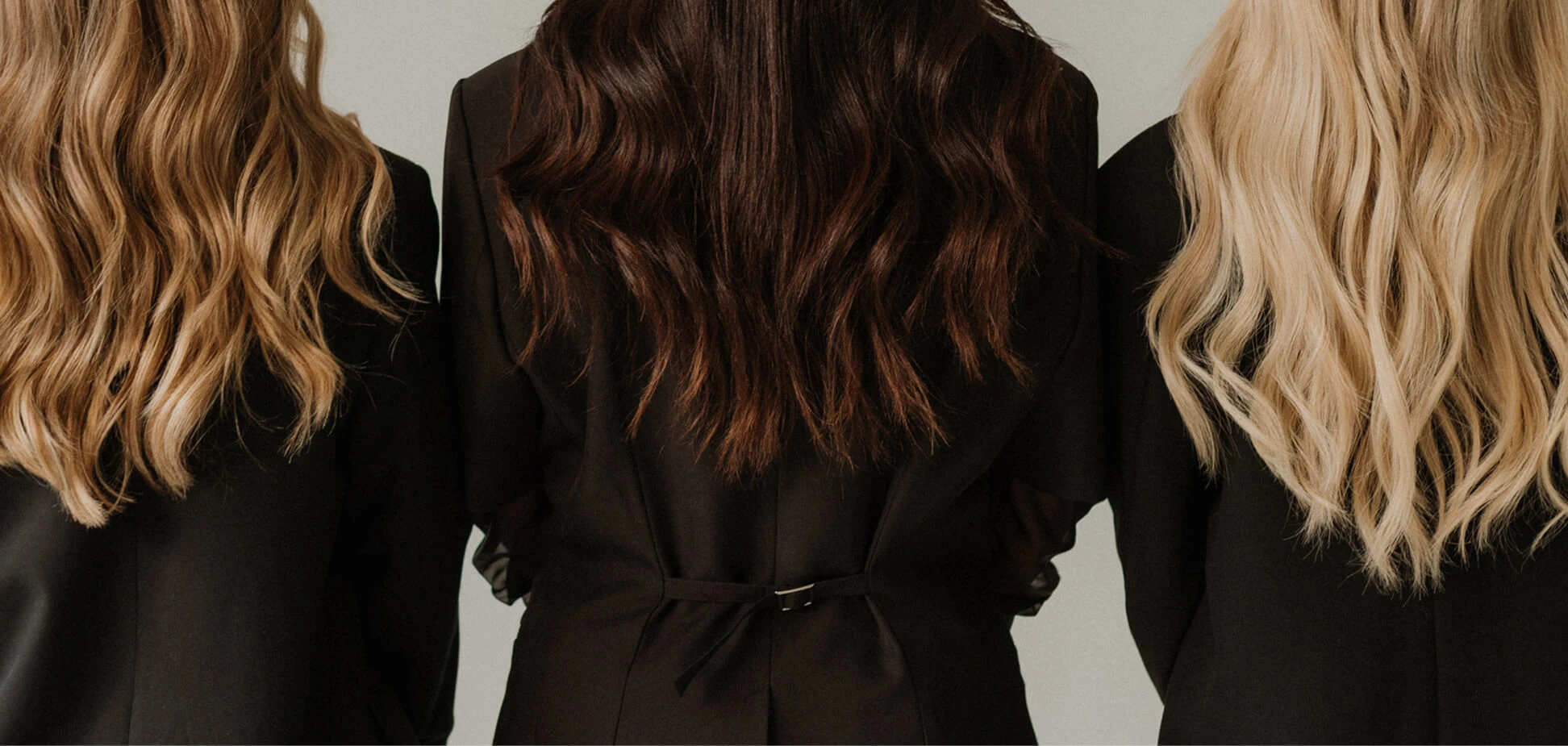 Three women shown from the back with wavy hair in blonde and brunette colors wearing black outfits.