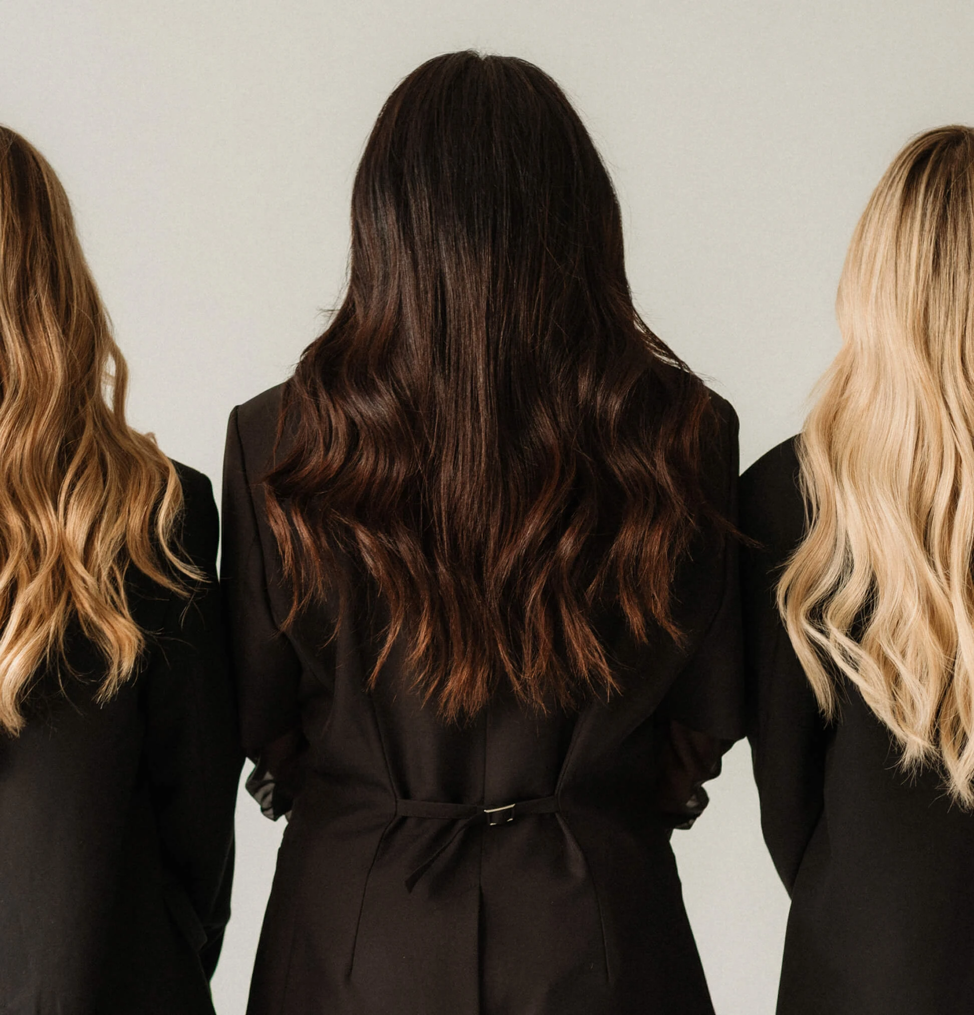 Back view of three women with long wavy hair in blond and brunette wearing black jackets.