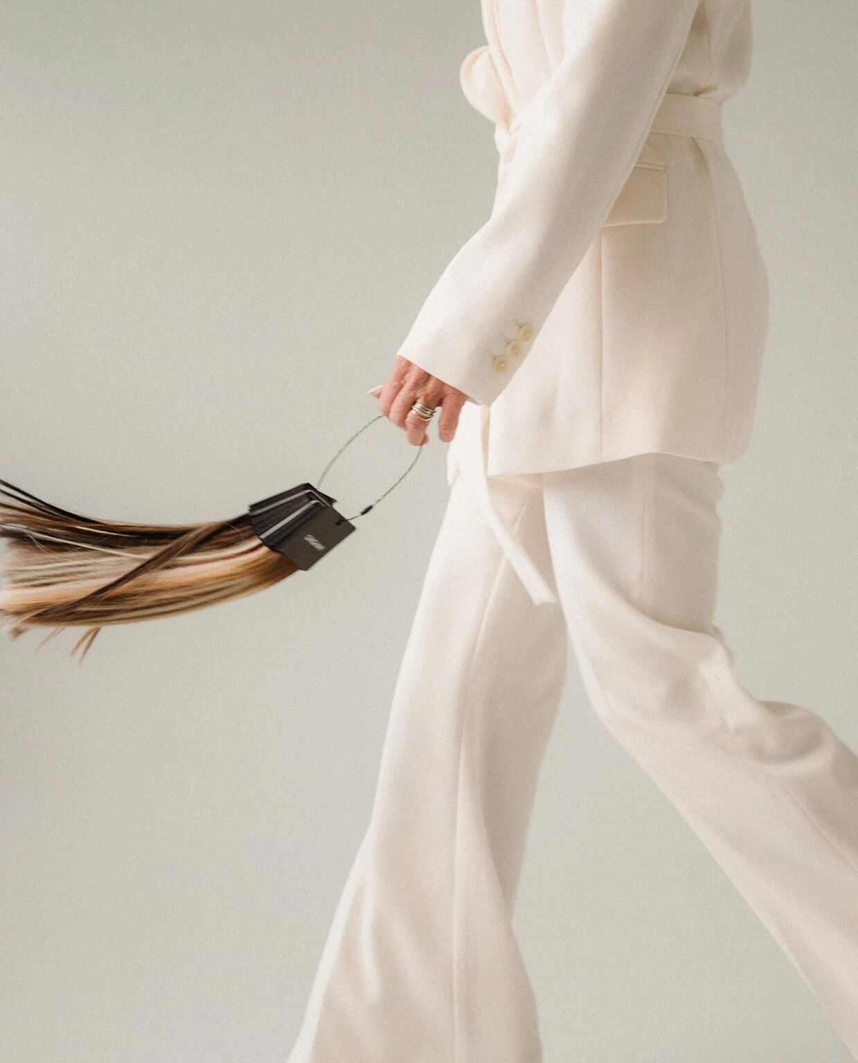 Person in a cream suit walking, holding a sample of hair color swatches in hand.