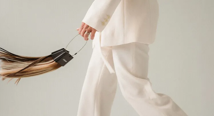 Person in white suit holding hair extensions with metal clasps in hand while walking.