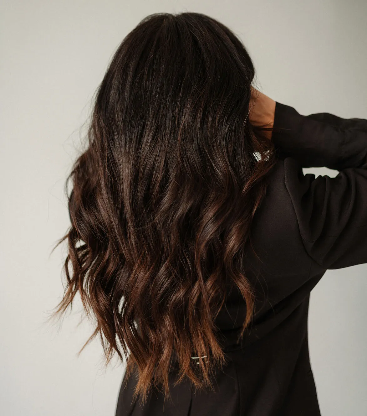 Person with long, dark wavy hair, wearing a black top, facing away from the camera.