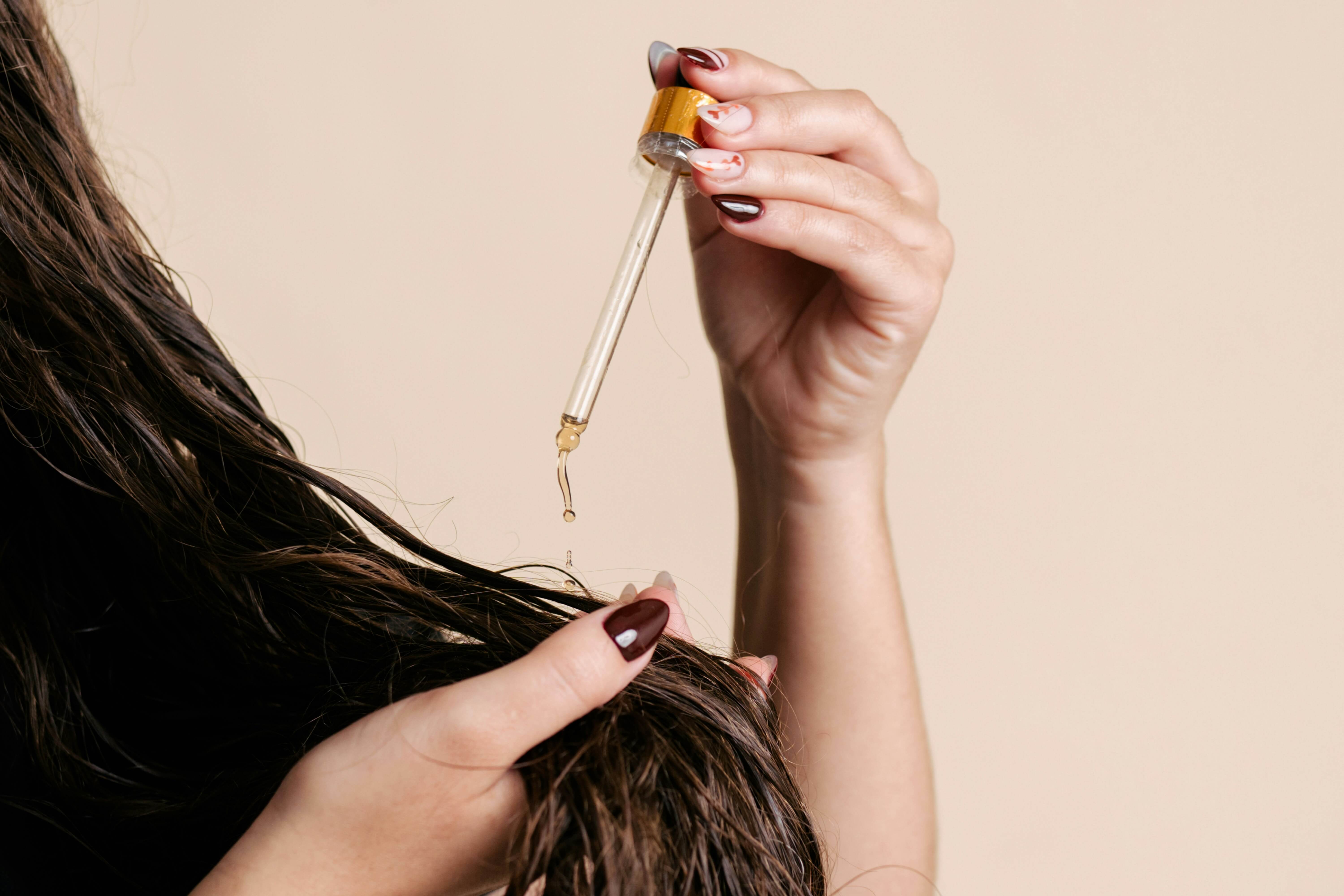 Applying nourishing hair oil to keep hair extensions healthy, soft, and hydrated between maintenance appointments.