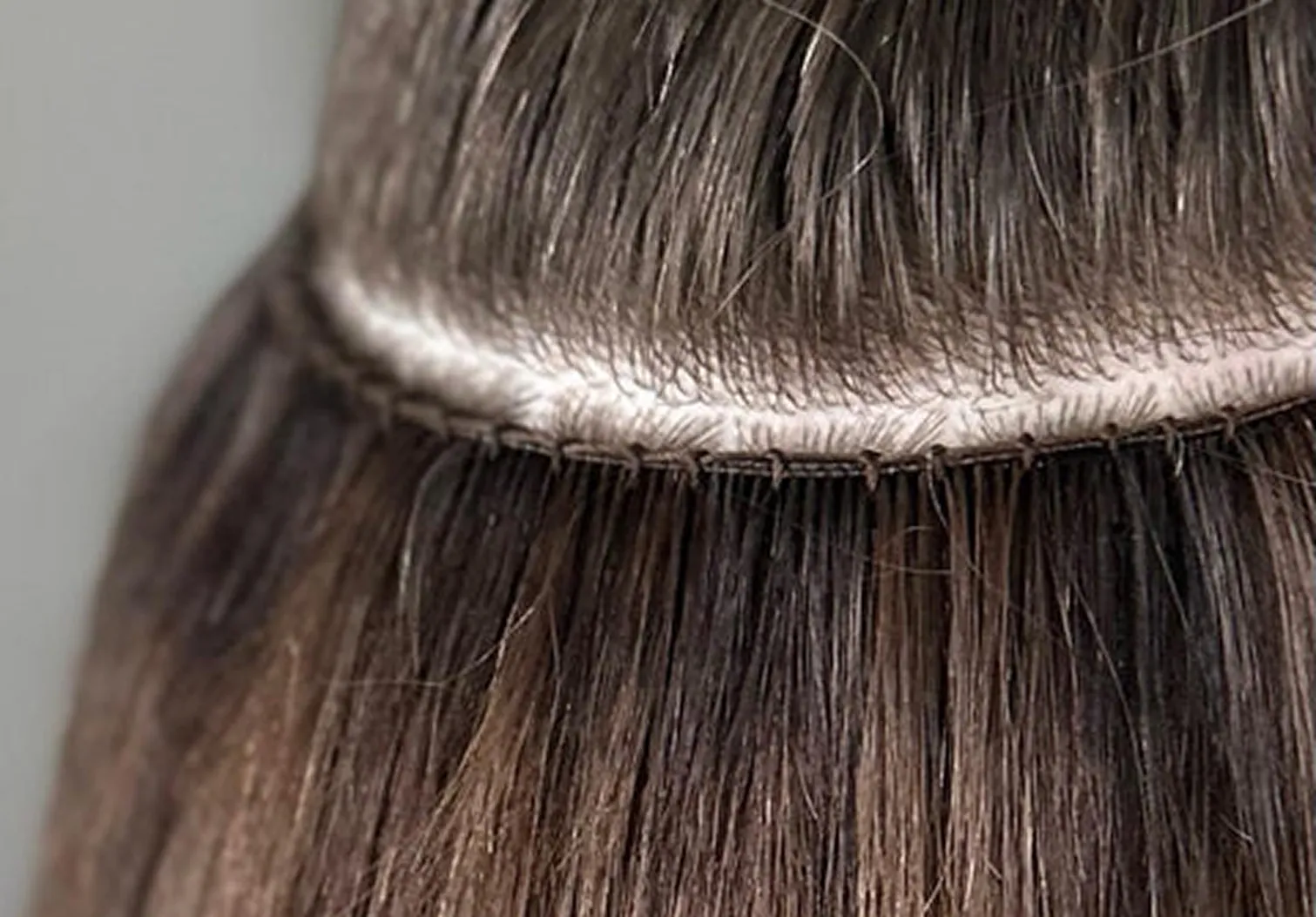 Close-up of a hand-tied hair extension weft sewn onto a beaded row for a seamless, natural-looking result.