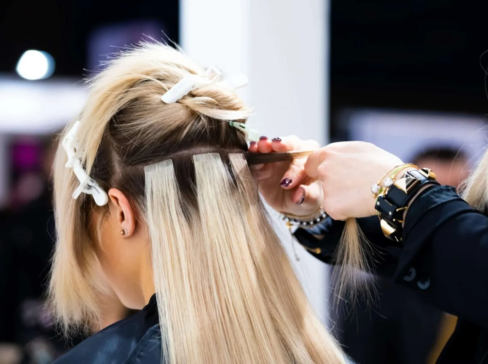 Stylist applying tape-in hair extensions section by section for added length and volume.