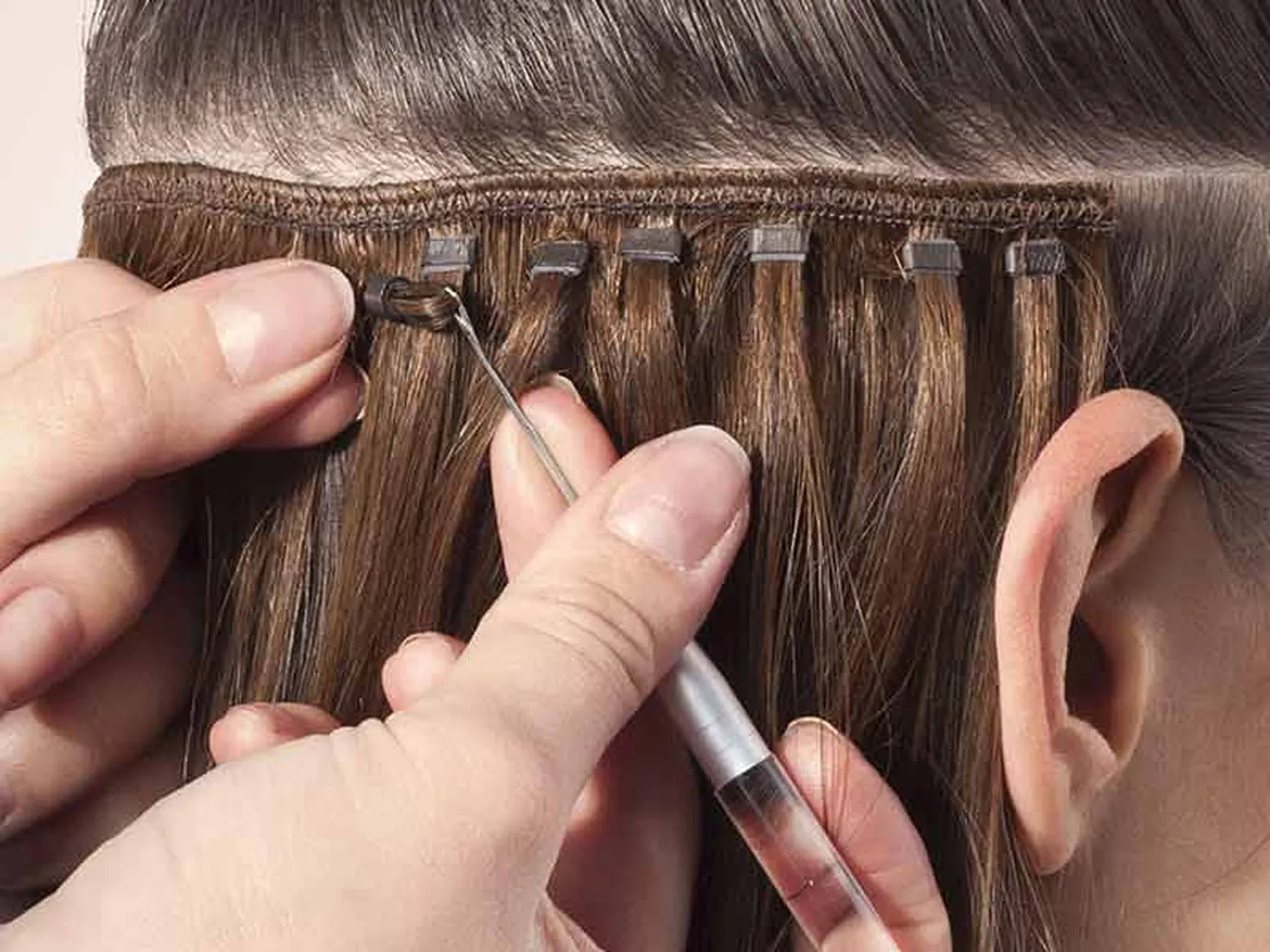 Close-up of sew-in hair extensions being stitched onto a braided foundation using a weaving needle.