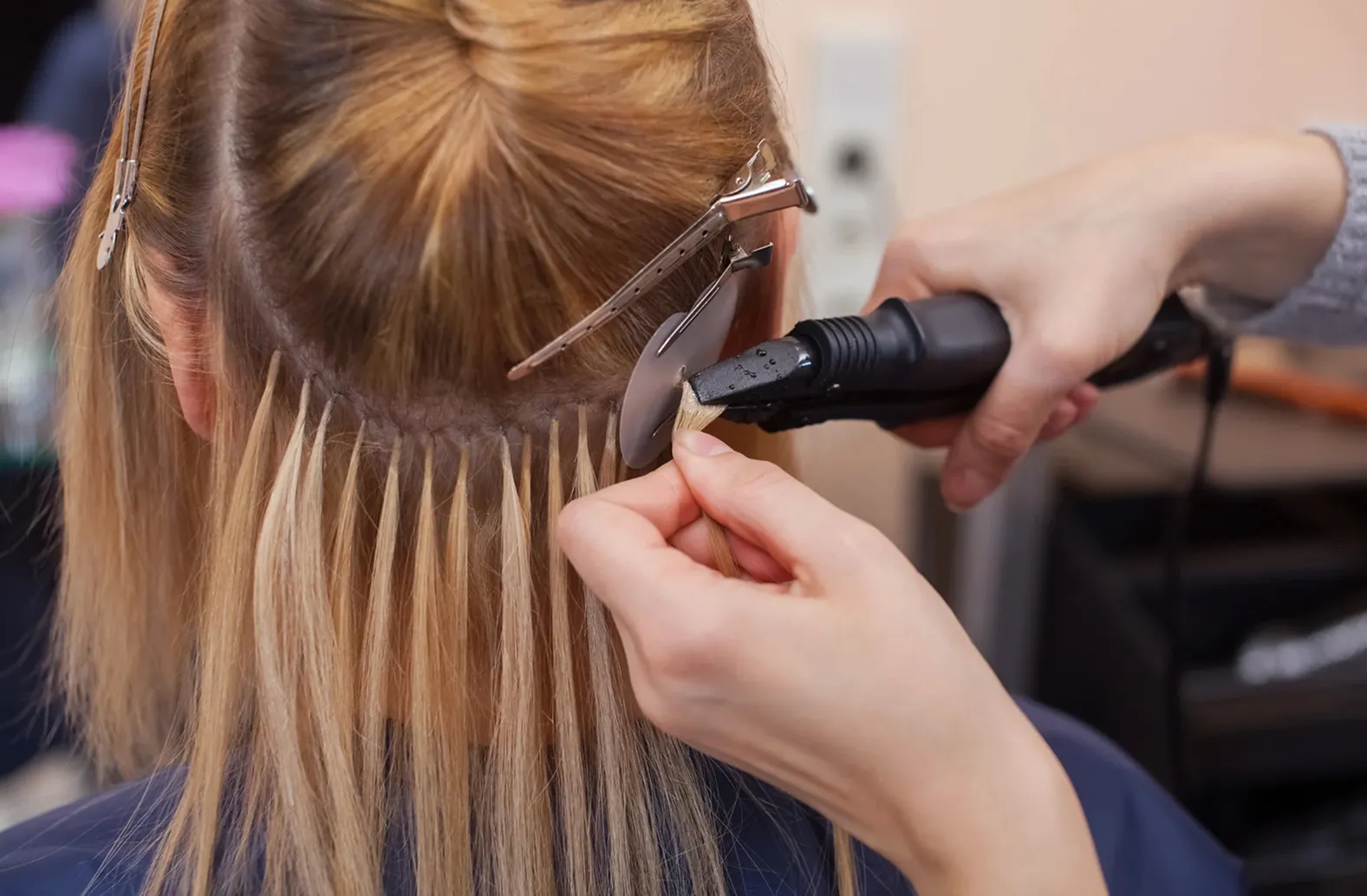 Stylist installing keratin bond hair extensions using a professional heat fusion tool.