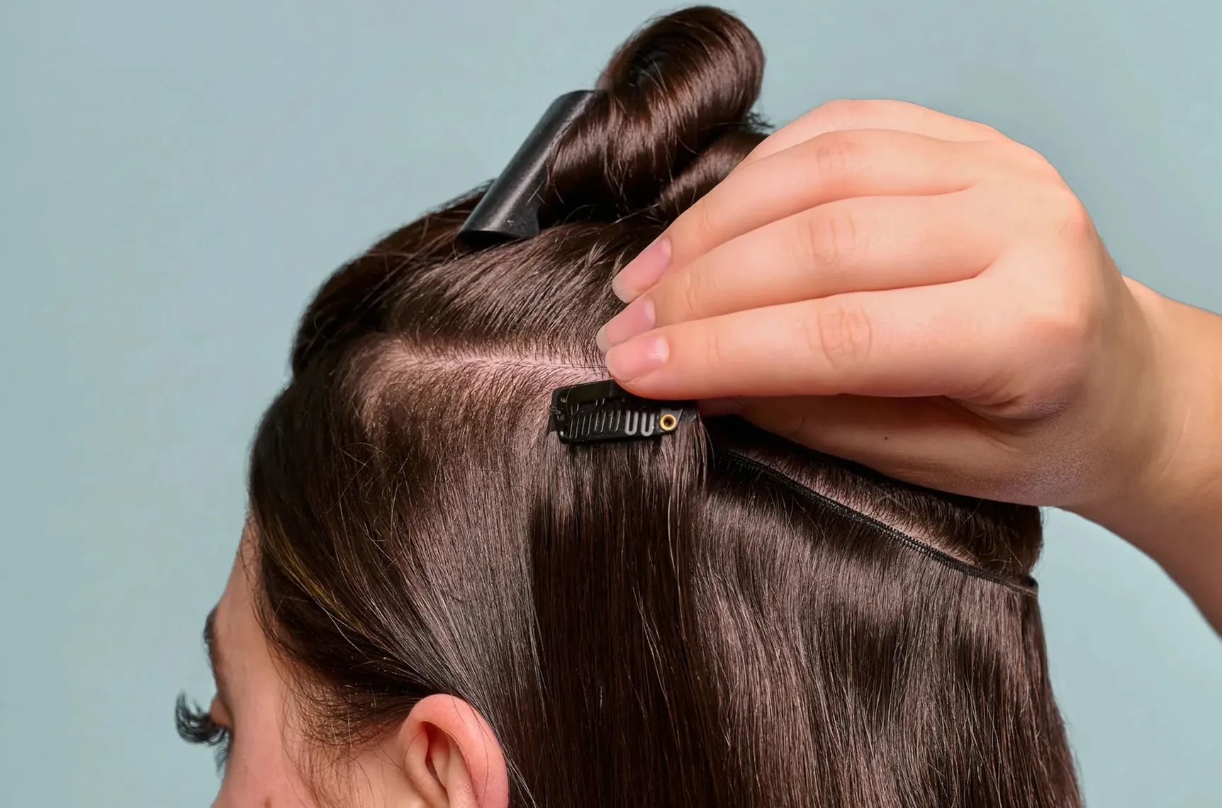 Stylist attaching a clip-in hair extension to natural hair for temporary length and volume.