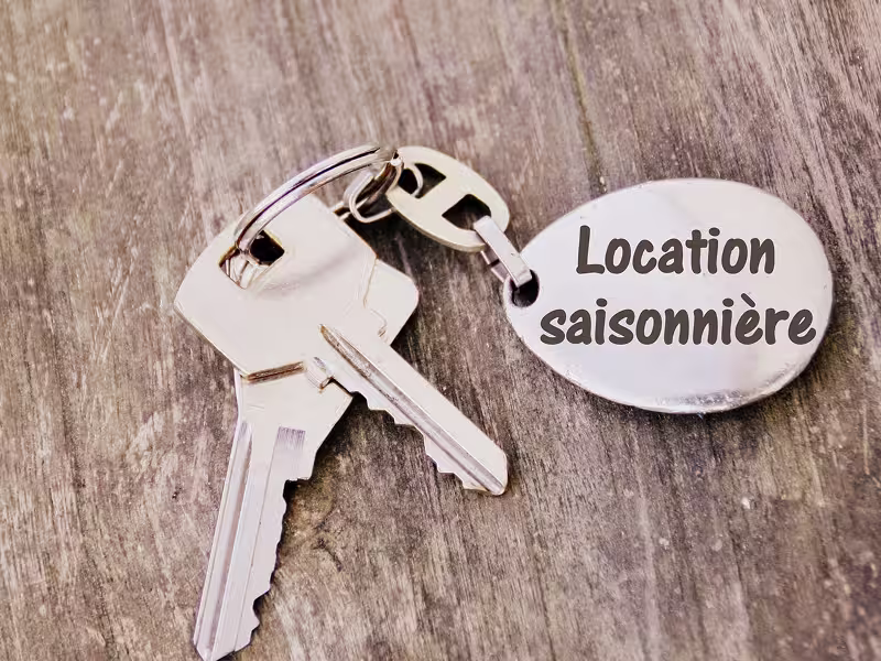 Juego de llaves con llavero «Location saisonnière» sobre una mesa de madera