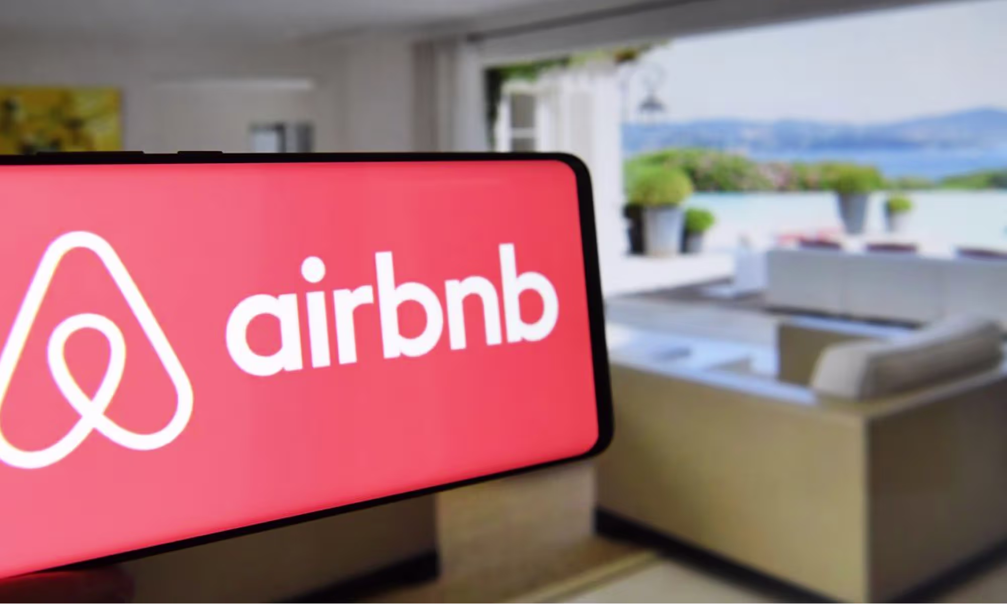 Smartphone con el logo de Airbnb en un salón con vista al mar