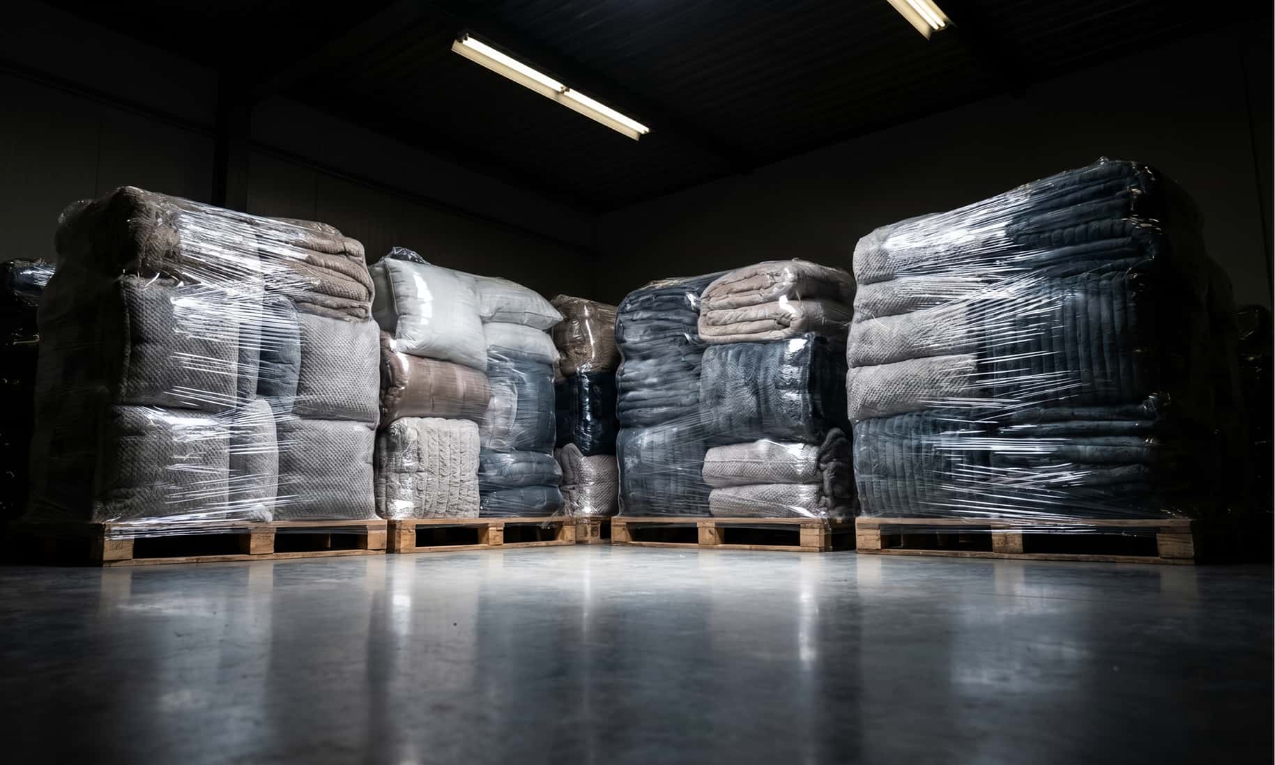 Αποθήκη της C&G Textiles με παλέτες έτοιμων υφασμάτων και λευκών ειδών, συσκευασμένα για διανομή.