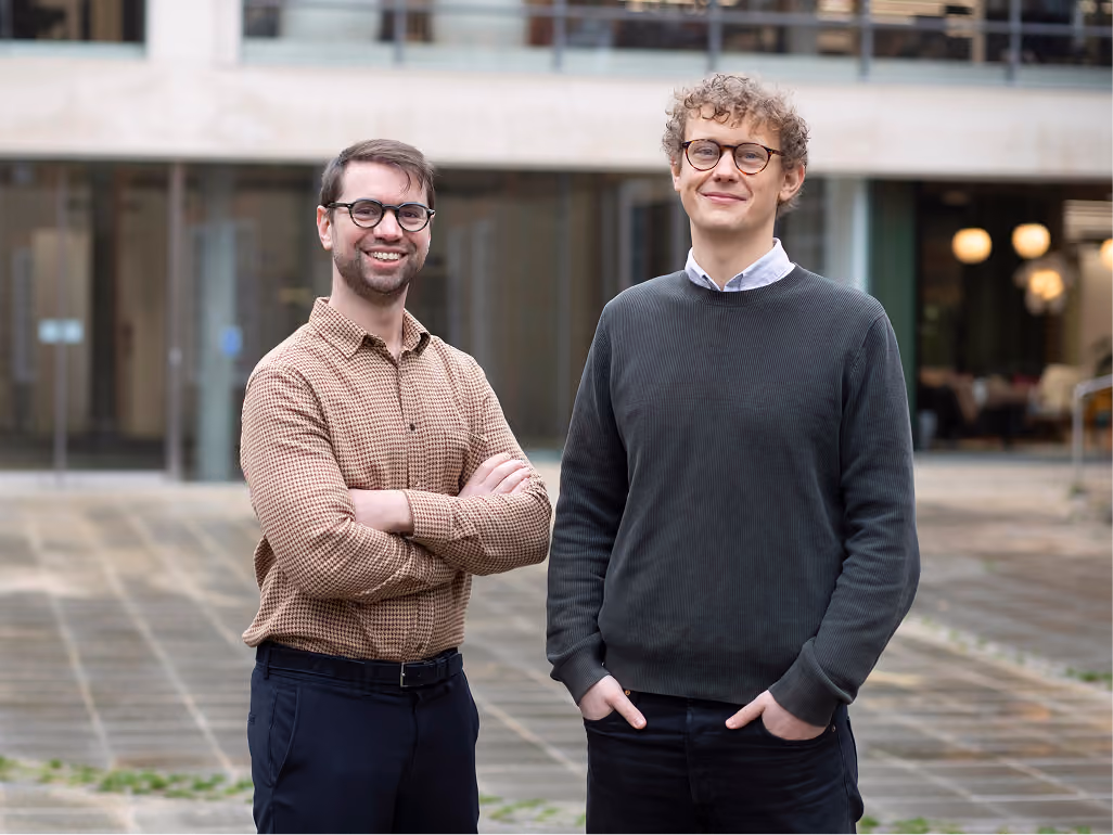Two men with glasses standing outside a modern building, smiling at the camera.